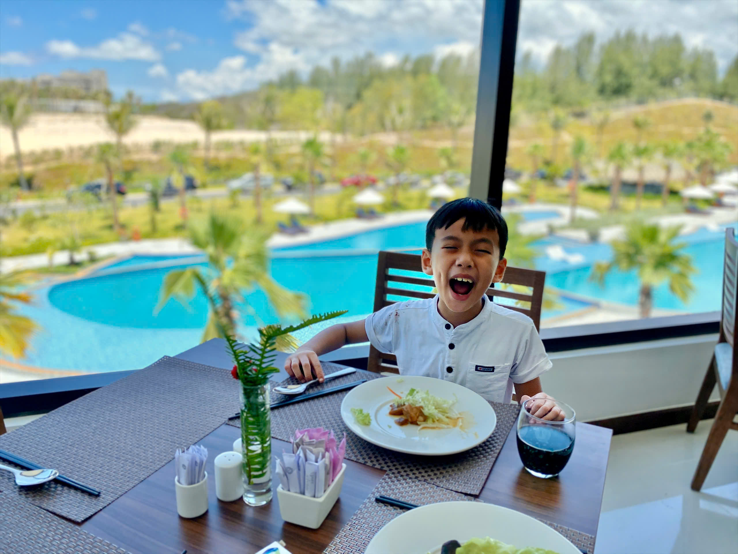 Bé trai cười tươi trong nhà hàng nhìn ra hồ bơi tại Cam Lâm